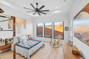 Bedroom with wood finished floors, ceiling fan, and a tray ceiling