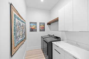 Laundry room with light wood-style floors, cabinet space, and washer and clothes dryer