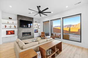Living area with a fireplace, light wood-style flooring, ceiling fan, built in features, and recessed lighting