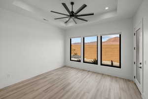 Unfurnished room with a tray ceiling, light wood finished floors, and ceiling fan
