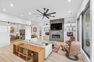 Living room featuring a barn door, a ceiling fan, light wood-type flooring, a fireplace, and built in features