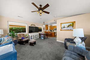 Living area with vaulted ceiling, carpet flooring, and a ceiling fan