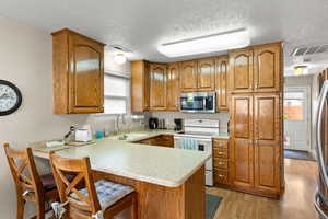 Kitchen with wood finish cabinetry, stainless steel appliances, a kitchen bar, a peninsula, and a textured ceiling