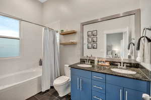 Bathroom with double vanity, tiled shower / bath, and dark tile patterned flooring
