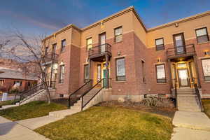 View of front facade featuring a balcony, a yard, brick siding, and stucco siding