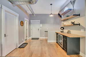 Bar area featuring wine cooler, butcher block counters, open shelves, light wood-style floors, and hanging light fixtures