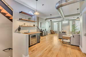 Indoor dry bar featuring light wood finished floors, beverage cooler, hanging light fixtures, and open shelves