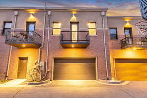 View of front of home featuring a balcony, an attached garage, brick siding, and stucco siding