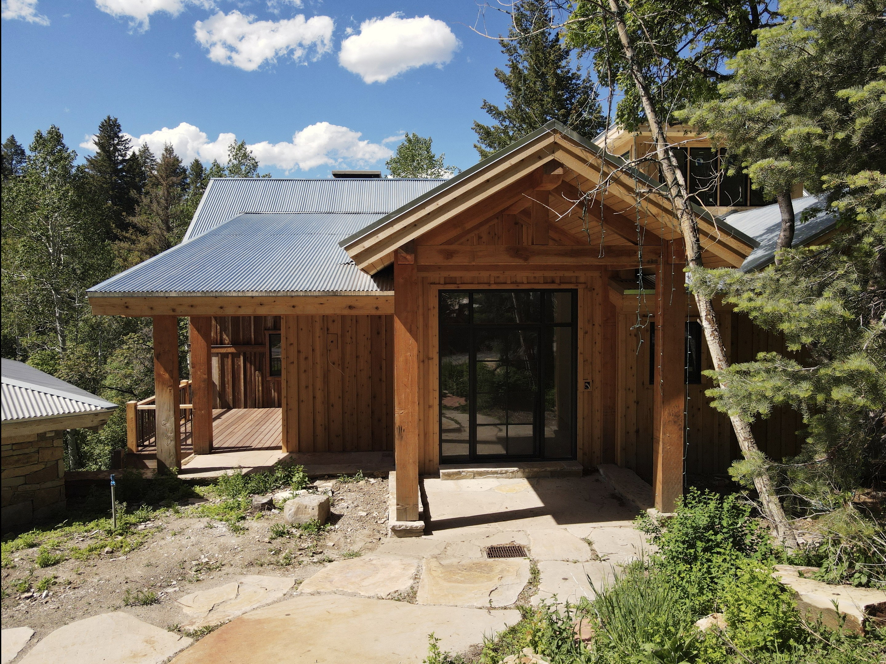 Wood-sided exterior featuring a corrugated metal roof, a covered entry with a solid wood door, and a stone slab pathway