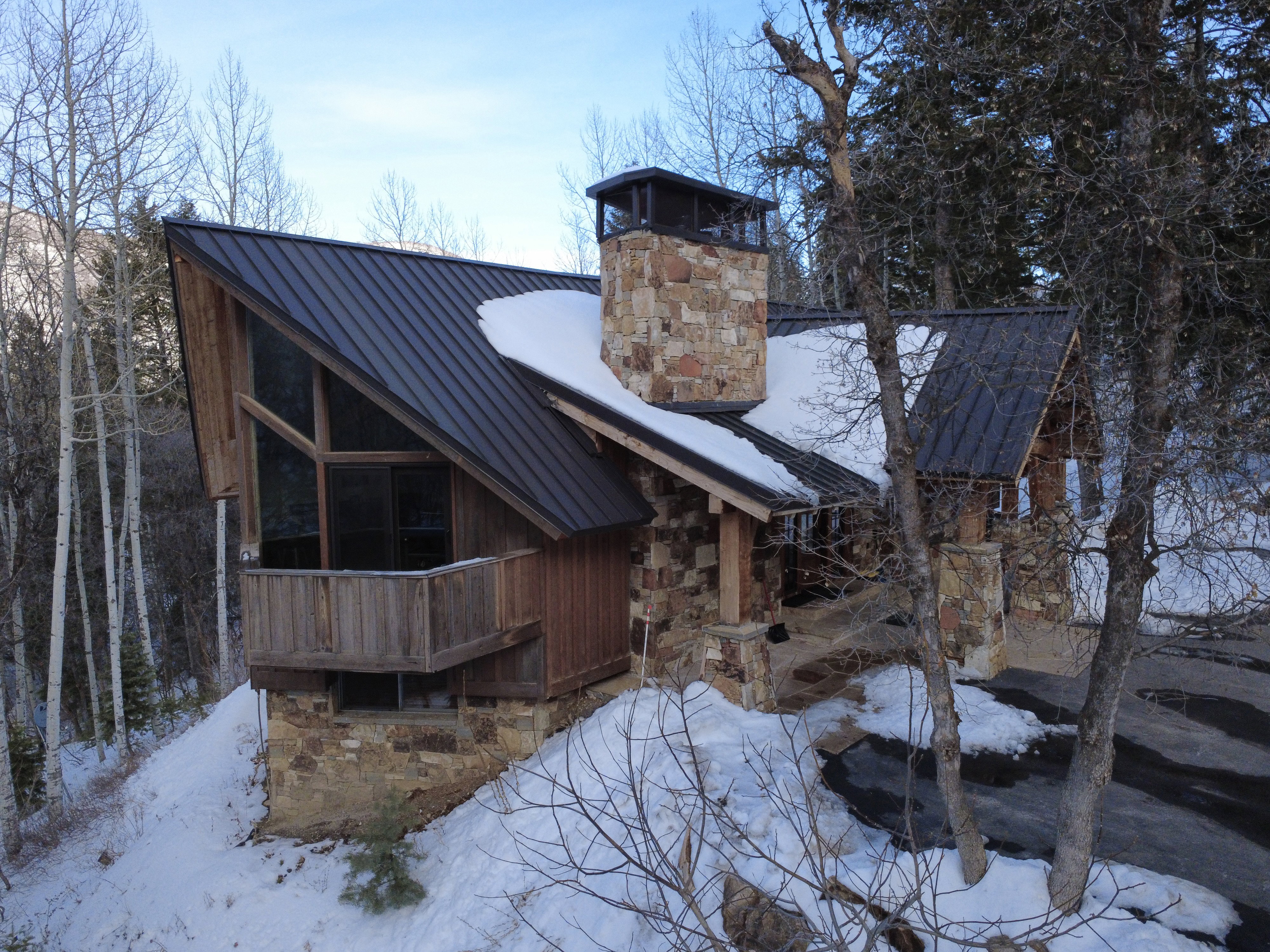 Snow covered property with stone siding, a standing seam roof, and a chimney
