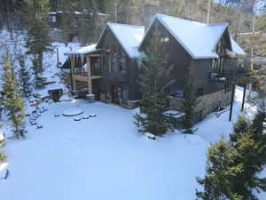 View of snow covered exterior with stone siding, a balcony, and view of scattered trees