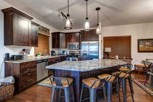Kitchen featuring dark wood finish cabinets, stainless steel appliances, pendant lighting, a breakfast bar, and dark wood finished floors