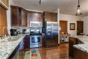 Kitchen featuring dark wood finish cabinetry, stainless steel appliances, light stone countertops, dark wood-style floors, and pendant lighting