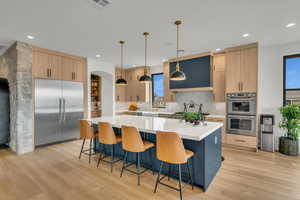 Two tone kitchen featuring stainless steel appliances, hanging light fixtures, a center island, modern cabinets, and light wood-style flooring
