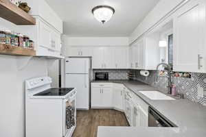 Kitchen with white appliances, open shelves, white cabinetry, laminate wood flooring, and backsplash