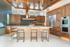 Kitchen with a kitchen breakfast bar with undercounter lighting, wood finish cabinets, stainless steel double oven, and wood drop ceiling