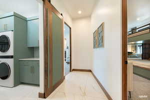 Main laundry area featuring a barn door, stacked washer / dryer, light finish flooring, and cabinet space