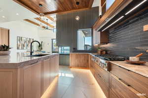 Kitchen with light stone counters, modern cabinets, decorative light fixtures, stainless steel stovetop, and wooden ceiling