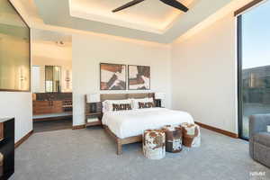 Carpeted bedroom with a ceiling fan, a raised ceiling, access to outside, and ensuite bathroom