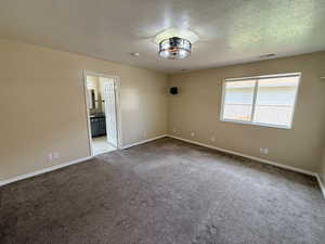Carpeted empty room with a textured ceiling and baseboards
