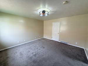 Empty room with a textured ceiling, dark carpet, and a smoke detector