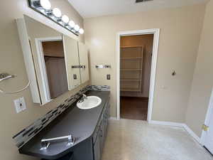 Full bath featuring a walk in closet, vanity, tasteful backsplash, and light flooring