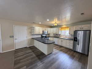 Kitchen featuring a peninsula, dark countertops, stainless steel appliances, open shelves, and a textured ceiling