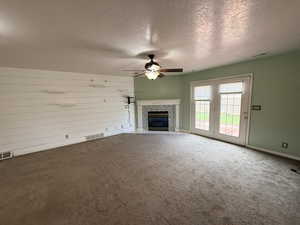 Unfurnished living room with a textured ceiling, a tile fireplace, a ceiling fan, and carpet floors