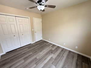 Unfurnished bedroom featuring a textured ceiling, dark wood-style floors, a closet, and a ceiling fan