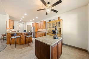 Kitchen with a peninsula, light stone countertops, a kitchen bar, a ceiling fan, and freestanding refrigerator