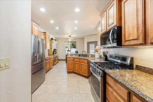 Kitchen with stainless steel appliances, light stone counters, a peninsula, a textured wall, and ceiling fan