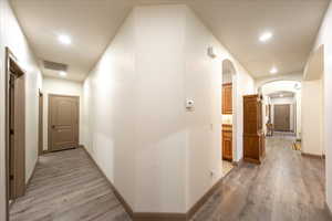 Hall featuring light wood finished floors, arched walkways, and recessed lighting