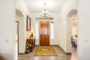Foyer with arched walkways, suspended lighting, and light wood finished floors