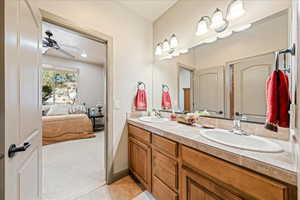 Ensuite bathroom featuring light carpet, double vanity, and ceiling fan