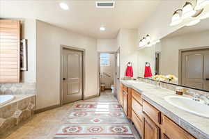 Bathroom featuring double vanity, tiled tub, light tile patterned floors, and recessed lighting
