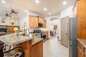 Kitchen featuring arched walkways, a ceiling fan, stainless steel appliances, open floor plan, and light stone countertops