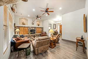 Living room with light wood-type flooring, a ceiling fan, hanging lights, a stone fireplace, and arched walkways