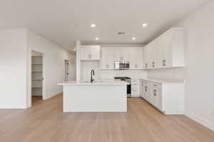 Kitchen featuring white cabinetry, stainless steel appliances, a kitchen island with sink, light wood-style flooring, and recessed lighting