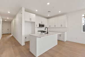 Kitchen featuring white cabinetry, light wood-style flooring, stainless steel appliances, a center island with sink, and recessed lighting
