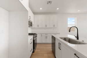 Kitchen featuring white cabinets, stainless steel appliances, light stone countertops, light wood-style floors, and recessed lighting