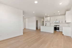 Kitchen featuring open floor plan, stainless steel appliances, white cabinetry, light countertops, and light wood-type flooring