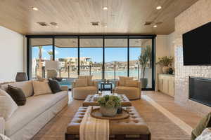 Living area with floor to ceiling windows, light wood-style flooring, wood ceiling, a large fireplace, and recessed lighting