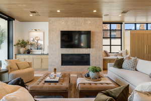 Living area featuring a large fireplace, light wood-style flooring, wooden ceiling, and floor to ceiling windows