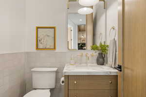 Half bath featuring vanity, tile walls, and a wainscoted wall