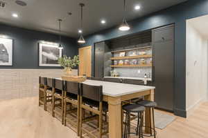 Indoor dry bar with pendant lighting, light countertops, gray cabinets, and light wood-style flooring
