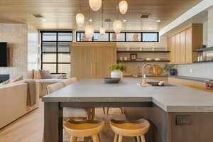 Kitchen with a breakfast bar, hanging light fixtures, open shelves, an island with sink, and wood ceiling