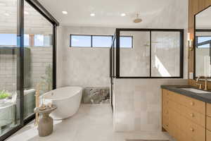 Bathroom featuring tile walls, vanity, a soaking tub, recessed lighting, and healthy amount of natural light