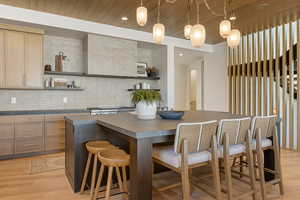 Kitchen with dark countertops, light wood-type flooring, open shelves, a kitchen bar, and wood ceiling