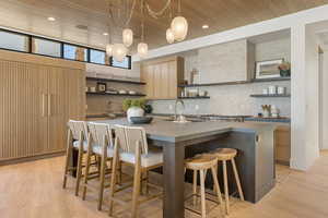 Kitchen with open shelves, a center island with sink, light wood-type flooring, a kitchen bar, and wooden ceiling