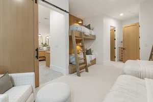 Bedroom with a barn door, ensuite bathroom, light colored carpet, and recessed lighting